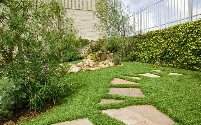 Artificial turf installed between natural stone steppers beside drought tolerant living planting in a Denver yard
